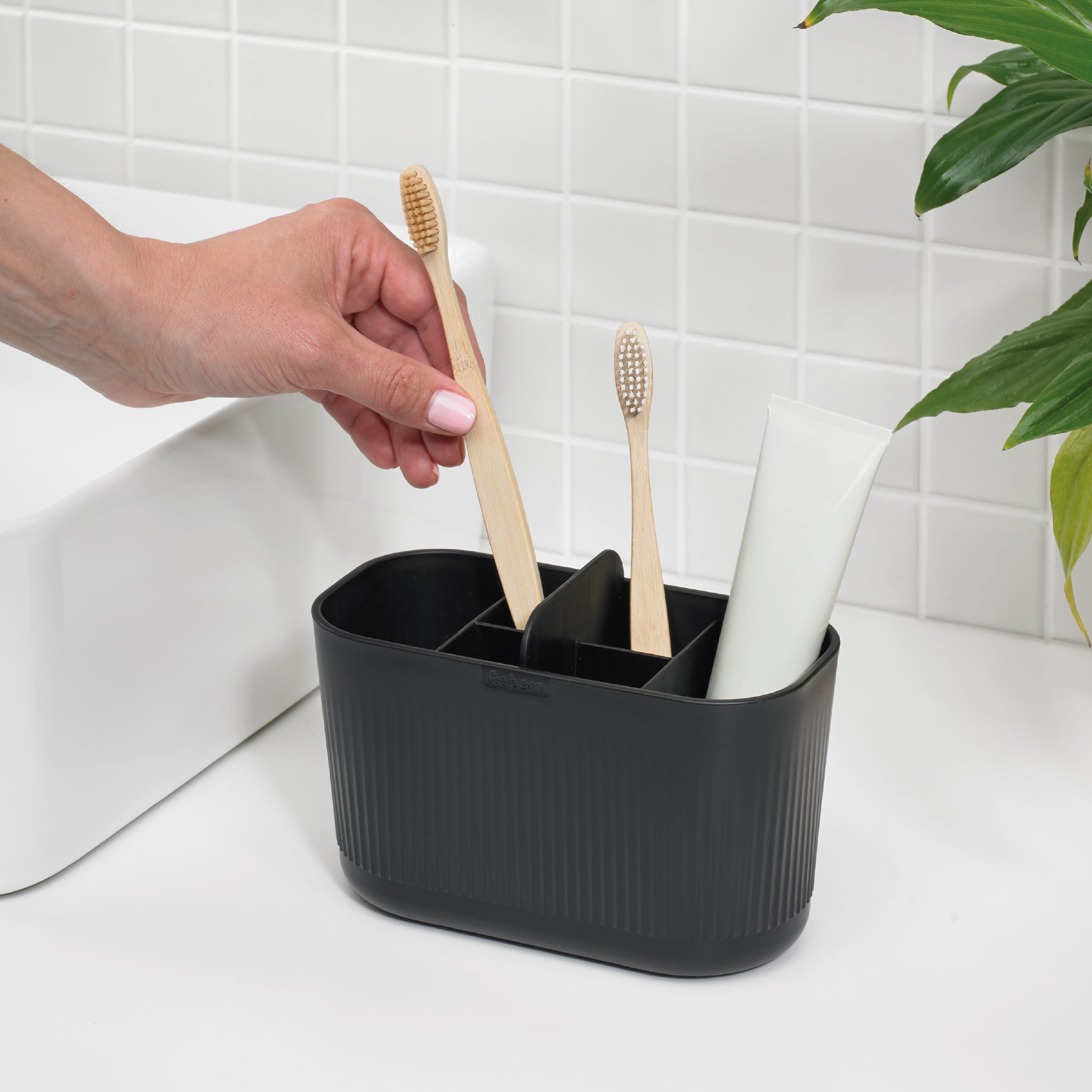 Black bathroom caddy with multiple compartments for organized storage of toothbrushes, toothpaste, and essentials.