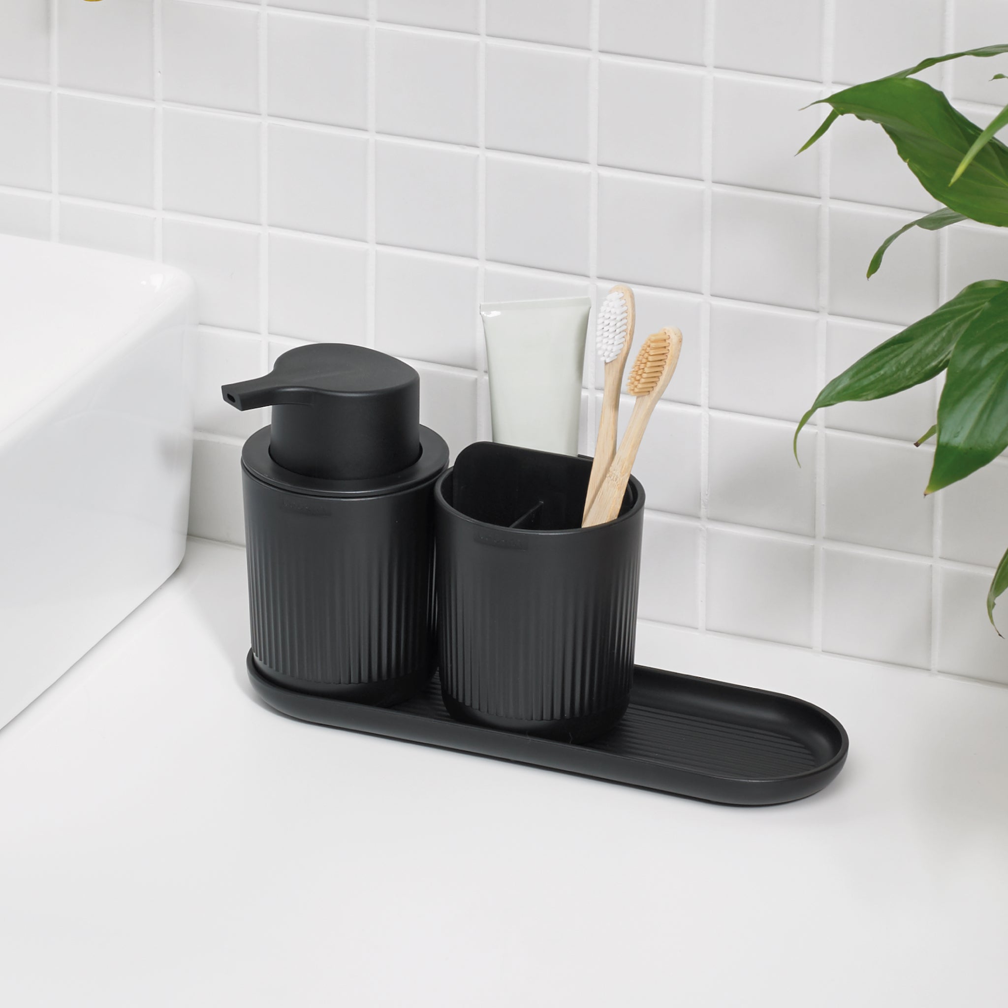 Sleek black bathroom set with ribbed texture, includes soap dispenser, toothbrush holder & tray for a modern, organized space.